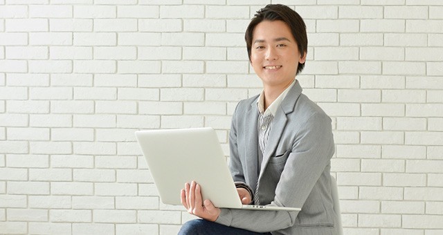 ノートパソコンを持ちながら微笑む男性
